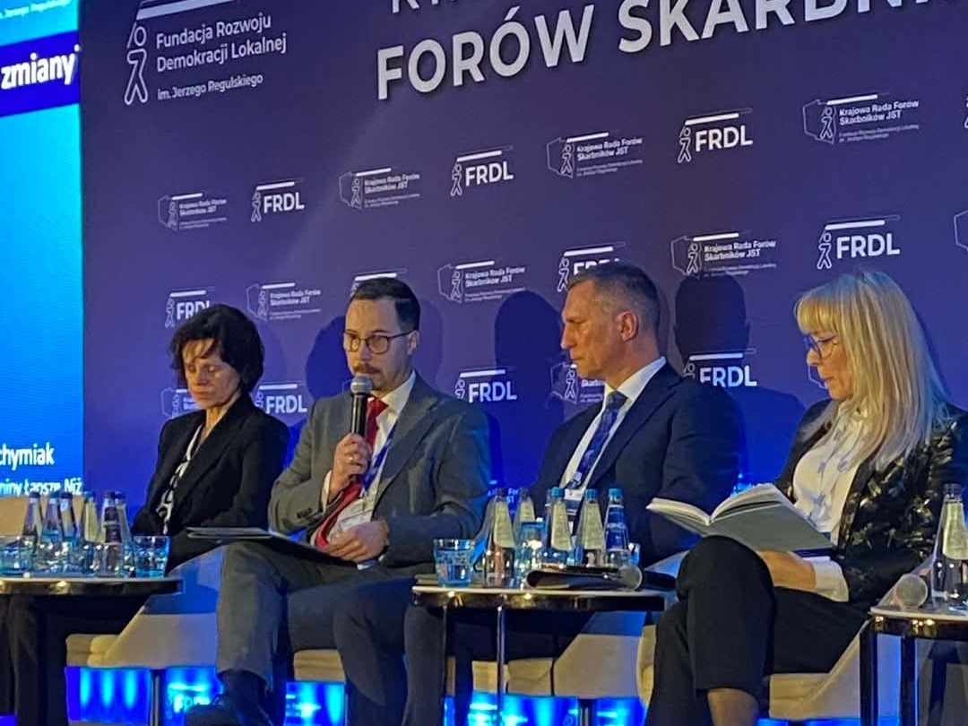 Przybliżona fotografia z VIII Krajowego Kongresu Forów Skarbników, widoczni są Hanna Majszczyk, Wiceminister, Podsekretarz Stanu w Ministerstwie Finansów, dr Daniel Budzeń, Ekspert Związku Miast Polskich, Fundacji Miasto i Fundacji Rozwoju Demokracji Lokalnej im. Jerzego Regulskiego ds. finansów lokalnych, Jacek Jachymiak, Skarbnik Gminy Łapsze Niżne oraz dr Julita Łukomska zastępczyni dyrektora NIST